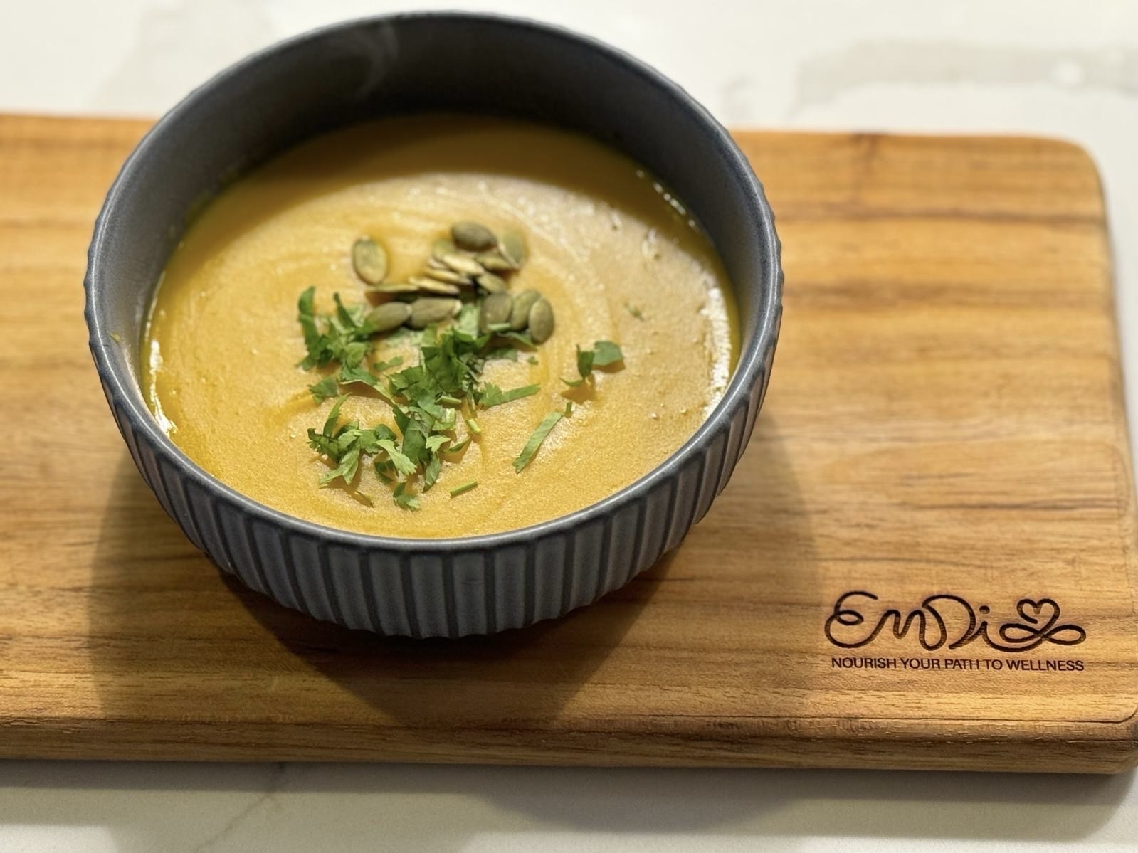 Plato de crema de calabaza sobre tabla de madera con el logo de Emdi Wellness grabado al lado